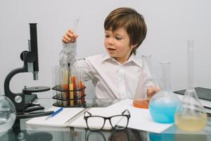 el chico con un microscopio y varios vistoso matraces en un blanco antecedentes. un chico haciendo experimentos en el laboratorio. explosión en el laboratorio. Ciencias y educación foto