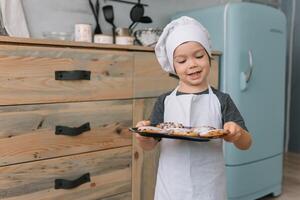 Young boy cute on the kitchen cook chef in white uniform and hat near table. Christmas homemade gingerbread. the boy cooked the chocolate cookies photo