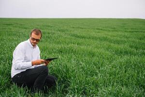 joven hermoso agrónomo, agricultura ingeniero en pie en verde trigo campo con tableta en manos en temprano verano. agronegocios concepto foto