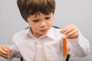 el chico con un microscopio y varios vistoso matraces en un blanco antecedentes. un chico haciendo experimentos en el laboratorio. explosión en el laboratorio. Ciencias y educación foto