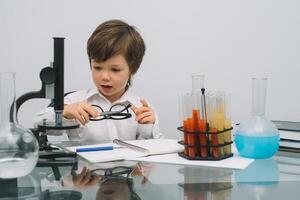 The boy with a microscope and various colorful flasks on a white background. A boy doing experiments in the laboratory. Explosion in the laboratory. Science and education photo