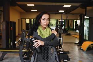 Young woman drinking water and taking a break after workout in gym photo