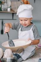 joven chico linda en el cocina cocinar cocinero en blanco uniforme y sombrero cerca mesa. hecho en casa pan de jengibre. el chico cocido el chocolate galletas foto