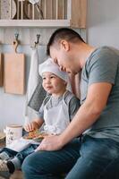 joven hombre y su hijo con horno sábana en cocina. padre con pequeño hijo en el cocina foto