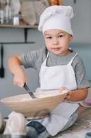 joven chico linda en el cocina cocinar cocinero en blanco uniforme y sombrero cerca mesa. hecho en casa pan de jengibre. el chico cocido el chocolate galletas foto