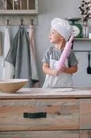 joven chico linda en el cocina cocinar cocinero en blanco uniforme y sombrero cerca mesa. hecho en casa pan de jengibre. el chico cocido el chocolate galletas foto