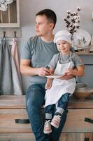 joven hombre y su hijo con horno sábana en cocina. padre con pequeño hijo en el cocina foto