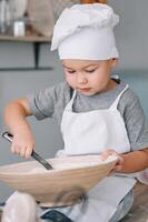 joven chico linda en el cocina cocinar cocinero en blanco uniforme y sombrero cerca mesa. hecho en casa pan de jengibre. el chico cocido el chocolate galletas foto