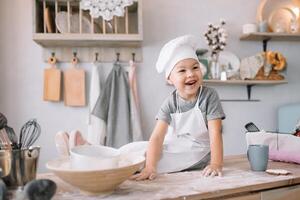 Young boy cute on the kitchen cook chef in white uniform and hat near table. homemade gingerbread. the boy cooked the chocolate cookies. photo