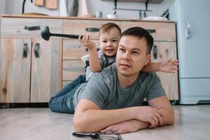 joven hombre y su hijo con horno sábana en cocina. padre con pequeño hijo en el cocina foto