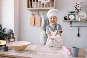 Young boy cute on the kitchen cook chef in white uniform and hat near table. homemade gingerbread. the boy cooked the chocolate cookies. photo