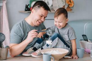 joven hombre y su hijo con horno sábana en cocina. padre con pequeño hijo en el cocina foto