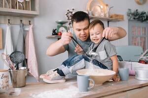 Young man and his son with oven sheet in kitchen. Father with little son on the kitchen. photo