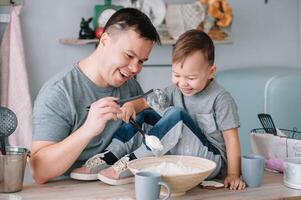 joven hombre y su hijo con horno sábana en cocina. padre con pequeño hijo en el cocina foto