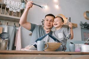 joven hombre y su hijo con horno sábana en cocina. padre con pequeño hijo en el cocina. foto