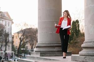 retrato de negocio mujer en sensación de concentrado estrés y ver estar y sostener el papel archivo sábana en el al aire libre peatonal caminar camino con el ciudad espacio de exterior moderno fachada edificio. foto