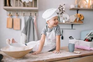 joven chico linda en el cocina cocinar cocinero en blanco uniforme y sombrero cerca mesa. hecho en casa pan de jengibre. el chico cocido el chocolate galletas. foto