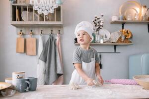 joven chico linda en el cocina cocinar cocinero en blanco uniforme y sombrero cerca mesa. hecho en casa pan de jengibre. el chico cocido el chocolate galletas. foto