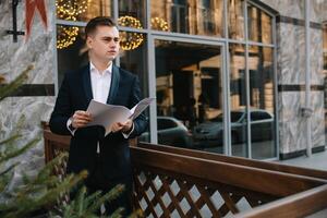 Young business man with documents and mobile phone near of modern building. photo