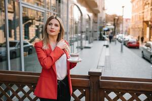 hermosa joven mujer de negocios con un desechable café taza, Bebiendo café, y participación tableta en su manos en contra urbano ciudad antecedentes foto