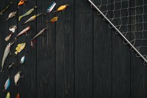 Fishing tackle - fishing spinning, hooks and lures on darken wooden background. Top view photo