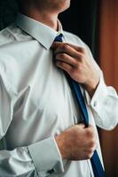 Groom's morning. Wedding preparing. Man in white shirt putting on cufflinks. Business dress code. photo