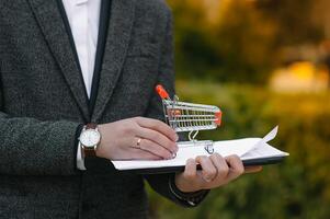 tienda de comestibles Tienda cadena gestión, venta al por menor y diario consumidor bienes comercio concepto. negocio hombre en un traje con un pequeño miniatura compras carro foto