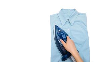 Female hand ironing clothes top view isolated on white background. Young woman with iron ironing man's shirt seen from above during housework. Blue iron on white table photo