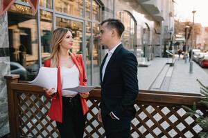 Preparation for meeting. Two young business people standing outside on the city street holding documents looking at each other smiling happy bottom view close-up. photo