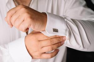 del novio Mañana. Boda preparando. hombre en blanco camisa poniendo en gemelos. negocio vestir código. foto