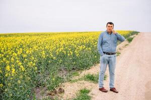 joven agrónomo en violación campo. agronegocios concepto. agrícola ingeniero en pie en un violación campo. foto