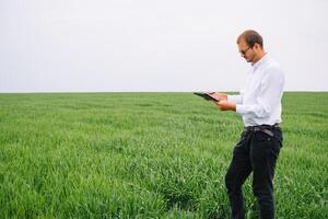 Young agronomist holds tablet touch pad computer in green wheat field. Agribusiness concept. agricultural engineer standing in a wheat field with a tablet in summer photo