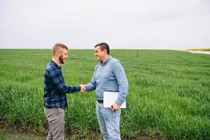 Two farmer standing in a green wheat field and shake hands. photo