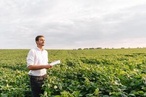 Young farmer in filed examining soybean corp. He is thumbs up. photo