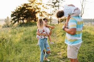 color foto de sonriente joven padres y dos niños, descanso y tener divertido en naturaleza. amar, familia y contento infancia estilo de vida concepto.