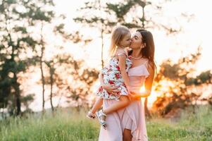 elegante madre y hermoso hija teniendo divertido en el naturaleza. contento familia concepto. belleza naturaleza escena con familia al aire libre estilo de vida. familia descansando juntos. felicidad en familia vida. madres día. foto