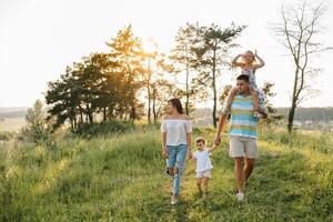 Color photo of smiling young parents and two children, rest and have fun in nature. Love, family and happy childhood lifestyle concept.