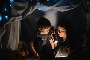 contento familia madre y niño hijo leyendo un libro con un Linterna en un tienda a hogar. familia concepto. foto