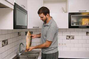 hombre corte Fresco pescado en cocina en hogar. hombre matanza pescado para cocinar. foto