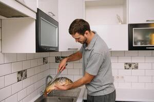 Man cutting fresh fish in kitchen in home. Man butchering fish for cook. photo