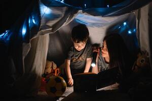 contento familia madre y niño hijo leyendo un libro con un Linterna en un tienda a hogar. familia concepto. foto