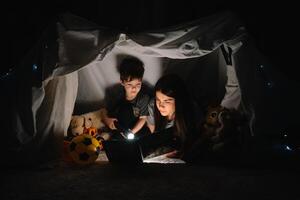 happy family mother and child son reading a book with a flashlight in a tent at home. family concept photo