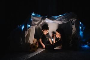 happy family mother and child son reading a book with a flashlight in a tent at home. family concept. photo