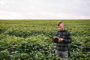 Young agronomist holds tablet touch pad computer in the soy field and examining crops before harvesting. Agribusiness concept. agricultural engineer standing in a soy field with a tablet in summer. photo