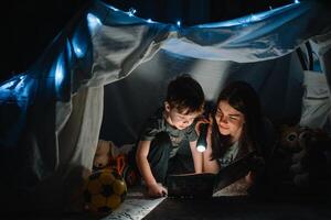 happy family mother and child son reading a book with a flashlight in a tent at home. family concept. photo