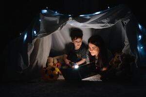 contento familia madre y niño hijo leyendo un libro con un Linterna en un tienda a hogar. familia concepto. foto