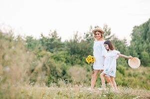 alegre madre y su pequeño hija teniendo divertido juntos en el verano antecedentes. contento familia en el naturaleza antecedentes. linda muchachas con vistoso flores foto