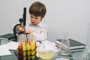 el chico con un microscopio y varios vistoso matraces en un blanco antecedentes. un chico haciendo experimentos en el laboratorio. explosión en el laboratorio. Ciencias y educación foto