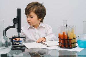 The boy with a microscope and various colorful flasks on a white background. A boy doing experiments in the laboratory. Explosion in the laboratory. Science and education photo