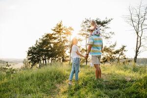 Happy family walking in the park. Mom, dad and daughter walk outdoors, parents holding the baby girl's hands. Childhood, parenthood, family bonds, marriage concept. photo